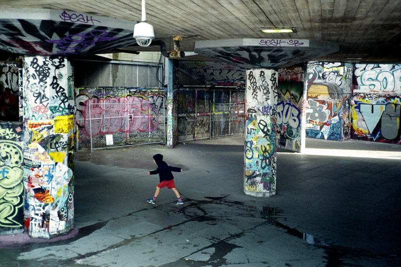 Photograph of a child walking past graffiti covered walls