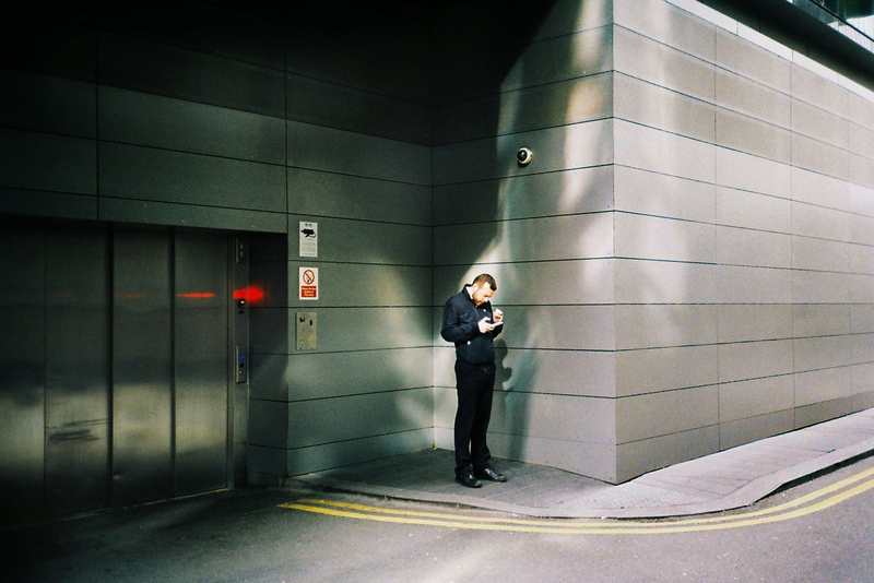 Photograph of a man smoking and checking his phone next to a fire exit